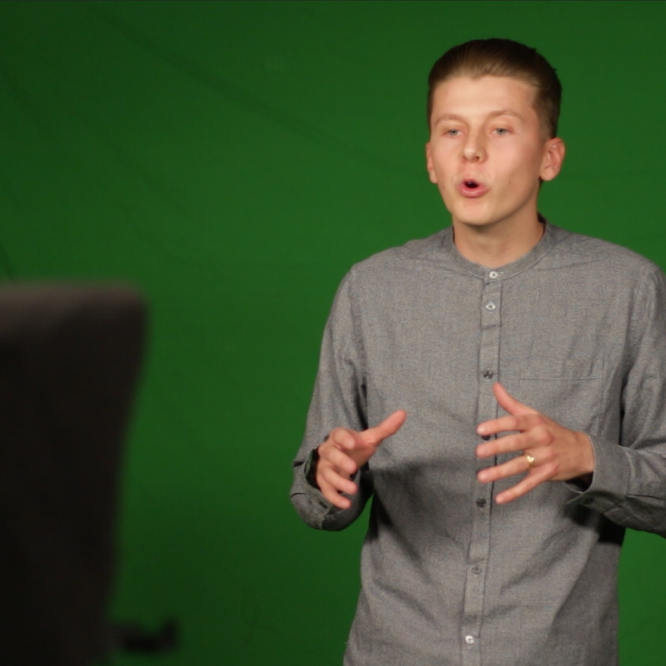 A photo of a team member explaining something with hand gestures in front of a greenscreen